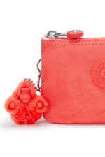 Kipling Creativity Small Purse. A small coral purse with zipper compartment, multiple inner compartments, Kipling logo, and monkey charm.