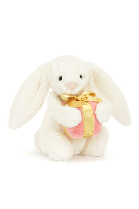 Jellycat Bashful Bunny With Present. A classic cream coloured bashful bunny with long floppy ears, fluffy tail, and pink present in arms.