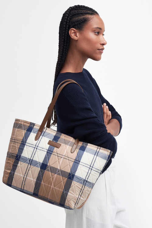 An image of a female model wearing the Barbour Wetherham Quilted Tartan Tote Bag in the colour Primrose Hessian.