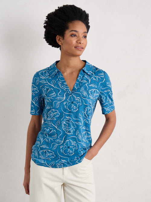 Seasalt Short Sleeve Misty Sky Shirt. A short sleeve T-shirt with collared V-neckline and all over camellia print on blue fabric.