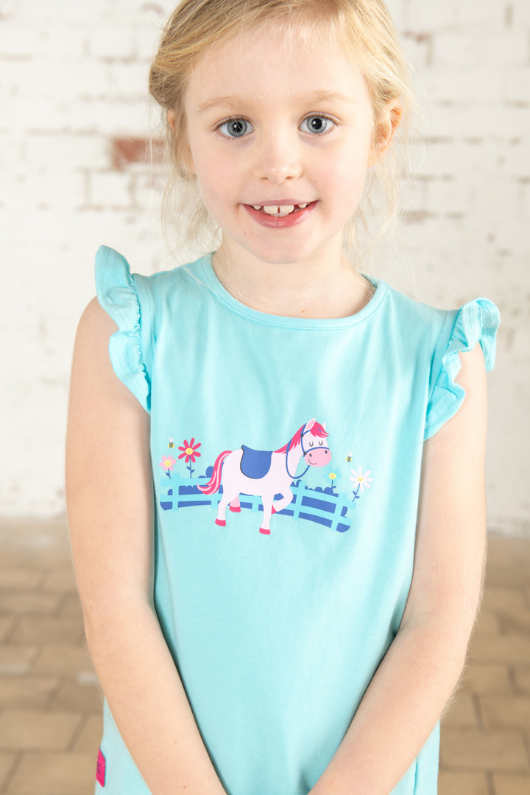 Lighthouse Causeway Swing Tee. A regular fit, kids t-shirt with short ruffle trim sleeves, a crew neck, and a sweet pony design on a light blue background.