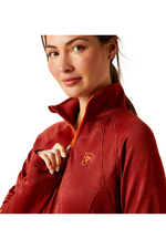 An image of a female model wearing the Ariat Tek Team 1/2 Zip Sweatshirt in the colour Fired Brick.