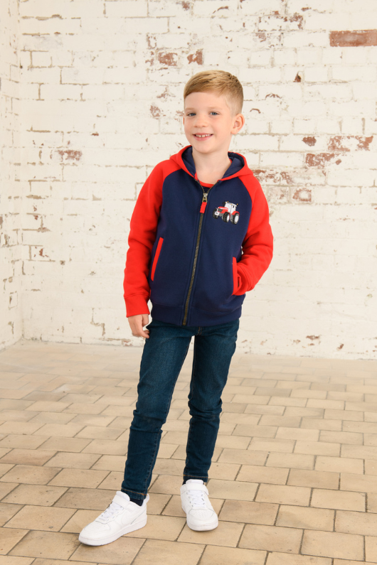 Lighthouse Jackson Full Zip Hoodie. A boys zip-up hoodie with waist pockets, a soft jersey lined hood, and a a navy torso with a tractor piqué on the chest and red sleeves.