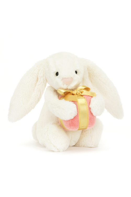 Jellycat Bashful Bunny With Present. A classic cream coloured bashful bunny with long floppy ears, fluffy tail, and pink present in arms.