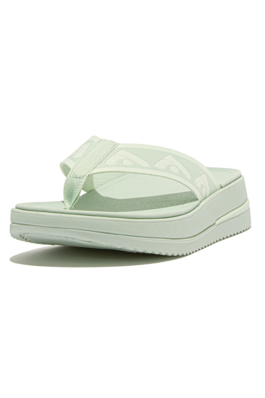 Fitflop Surff Webbing Toe Post Sandals. A pair of sage green sandals with cushioned sole, wedge heel, and wide patterned strap.