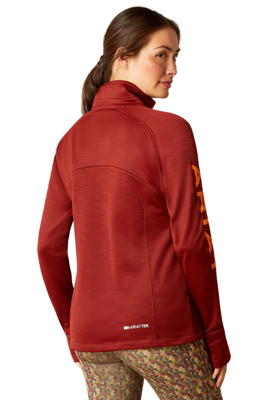 An image of a female model wearing the Ariat Tek Team 1/2 Zip Sweatshirt in the colour Fired Brick.