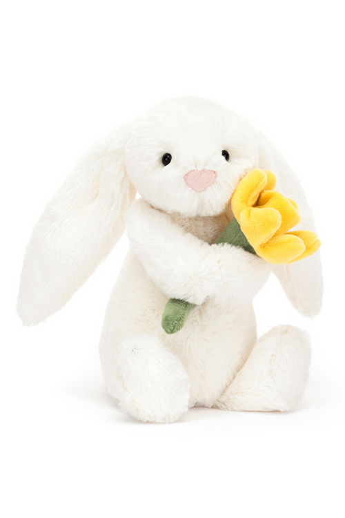 Jellycat Daffodil Bunny Little. A cream coloured bunny soft toy holding a yellow daffodil.