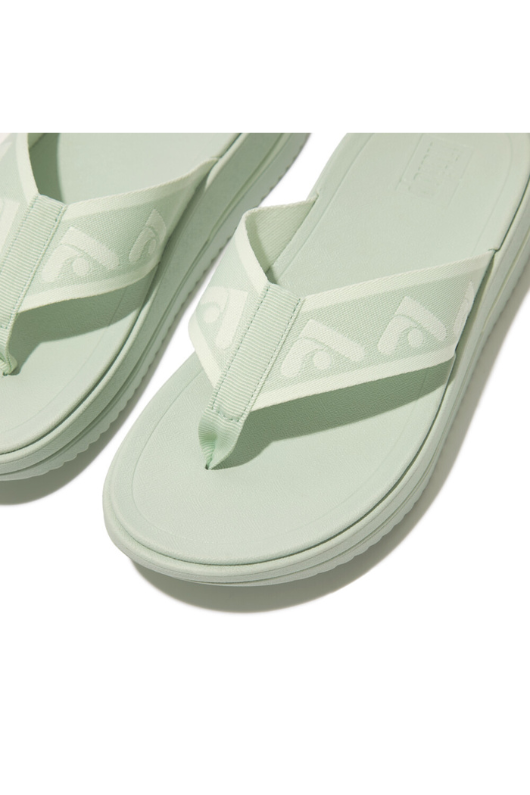 Fitflop Surff Webbing Toe Post Sandals. A pair of sage green sandals with cushioned sole, wedge heel, and wide patterned strap.