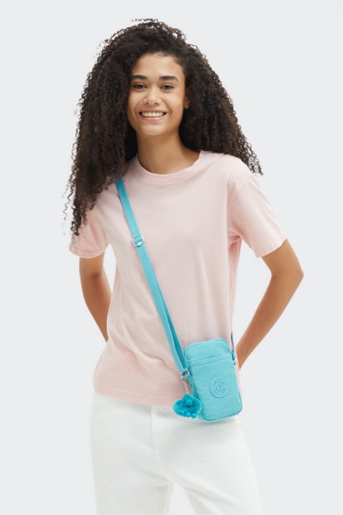 An image of a female model wearing the Kipling Tally Phone Bag in the colour Deepest Aqua.
