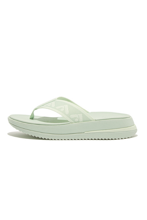 Fitflop Surff Webbing Toe Post Sandals. A pair of sage green sandals with cushioned sole, wedge heel, and wide patterned strap.