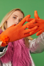 An image of a female model wearing the Jayley Suede Faux Pom Glove in the colour Tangerine.