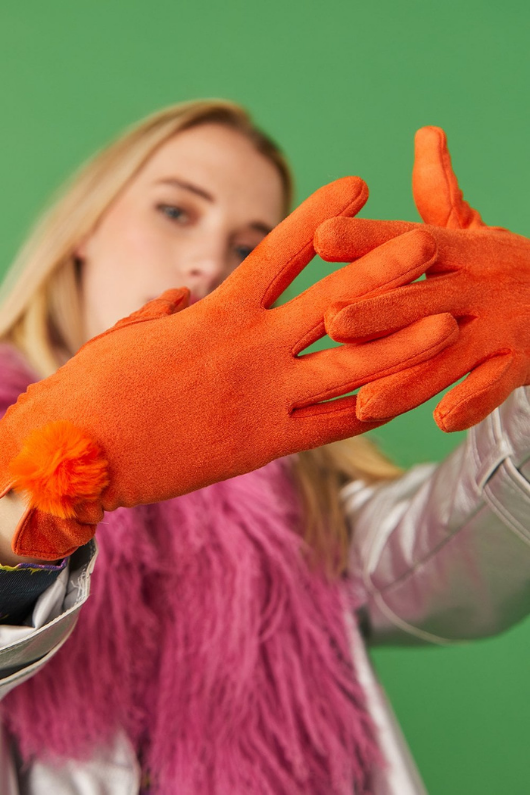 An image of a female model wearing the Jayley Suede Faux Pom Glove in the colour Tangerine.