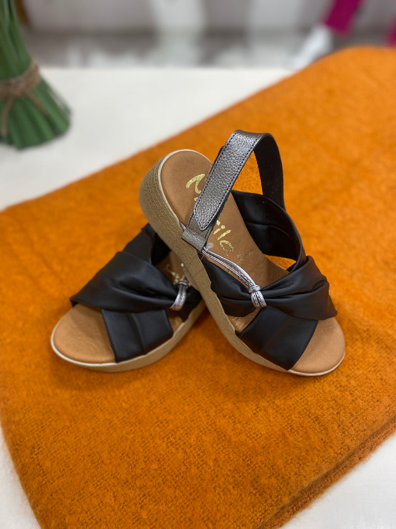 Marila Sling Back Sandal. A pair of low wedge sandals with black cross-over strap design and shiny heel strap.