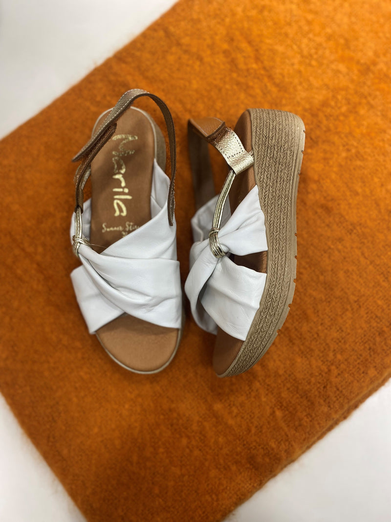 Marila Sling Back Sandal. A pair of low wedge sandals with white cross-over strap design and shiny heel strap.