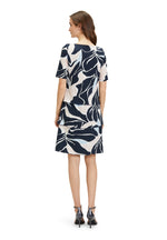 Betty Barclay Tiered Dress. A knee-length straight fit dress, with mid-length sleeves. This dress features an abstract print with pastel blue and pink accents on a navy background.