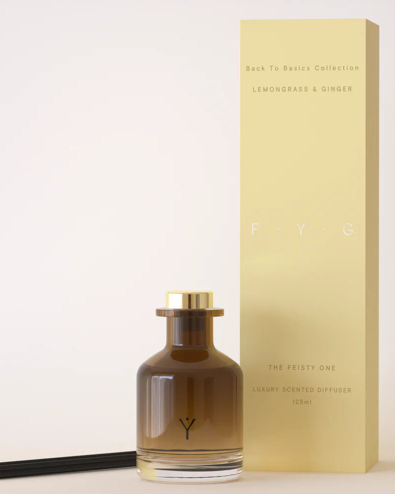 Fragrance diffuser bottle with gold cap and packaging on a light background