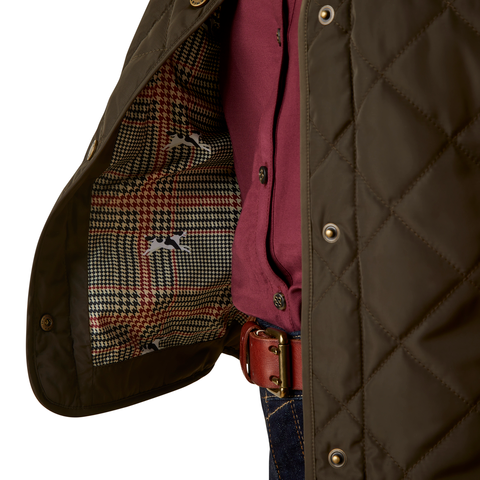 An image of a female model wearing the Ariat Woodside Quilted Gilet in the colour Earth.