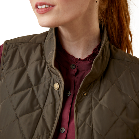 An image of a female model wearing the Ariat Woodside Quilted Gilet in the colour Earth.