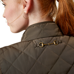 An image of a female model wearing the Ariat Woodside Quilted Gilet in the colour Earth.