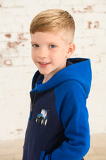 Lighthouse Jackson Full Zip Hoodie. A boys zip-up hoodie with waist pockets, a soft jersey lined hood, and a a navy torso with a tractor piqué on the chest and blue sleeves.