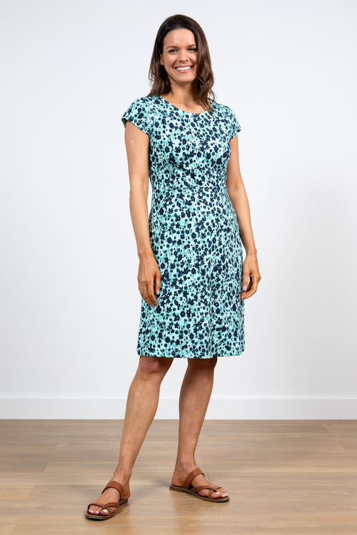 Lily & Me Harbourside Dress Confetti. A knee-length dress with short cap sleeves, a feminine round neckline, inverted pleats at the waist, and a turquoise design with black flower detail.