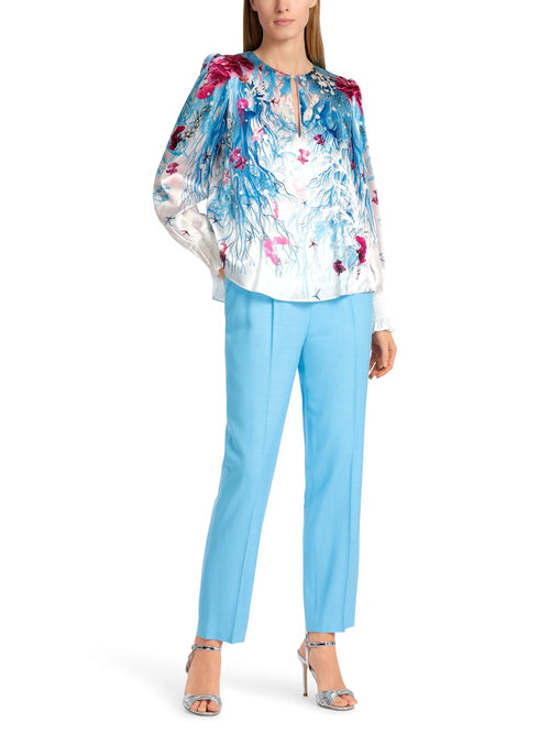 Marc Cain Long Sleeve Pattern Blouse. A relaxed fit blouse with long sleeves, featuring a ruffle detail. This top has a round neck with slit detail and back zip. The design has an underwater themed print in a mix of blue and red.