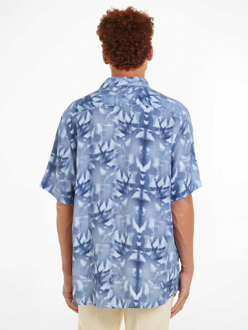 An image of a model wearing the Tommy Hilfiger Palm Print Tie-Dye Linen Relaxed Short Sleeve Shirt in the colour Well Water.