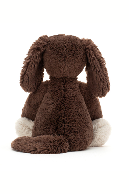 Jellycat Bashful Fudge Puppy. A cuddly toy dog with brown and white fur, floppy ears and long tail.